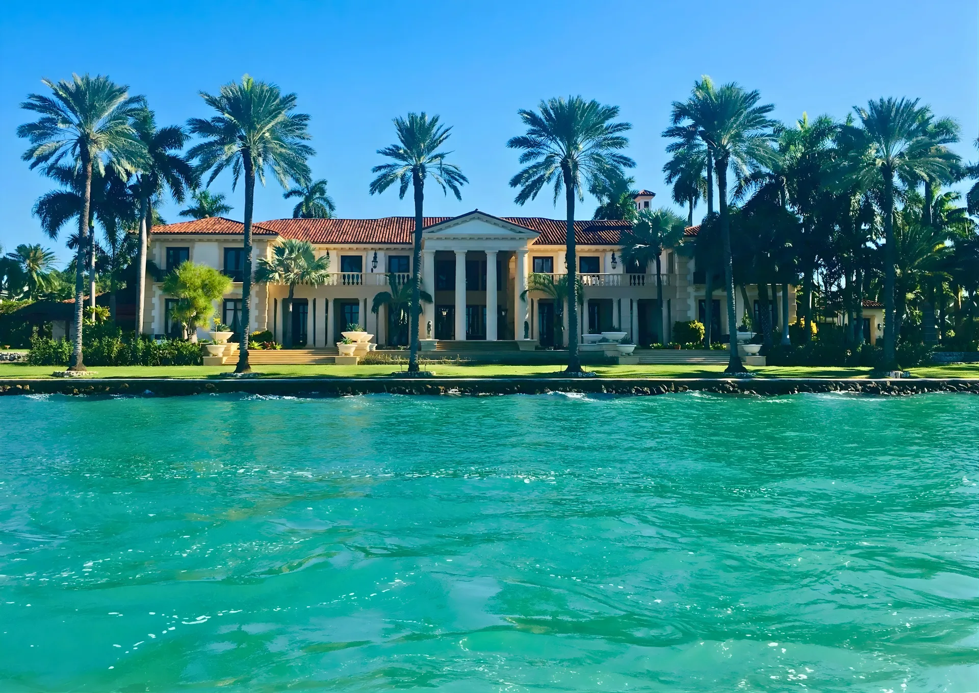 Palm-lined waterfront estate viewed across turquoise water